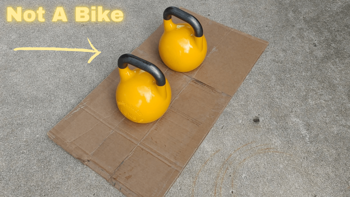 Photo of two 16kg kettlebells on cardboard to protect concrete underneath. The kettlebells are yellow and competition style. The handles gleam slightly in the sunlight.
